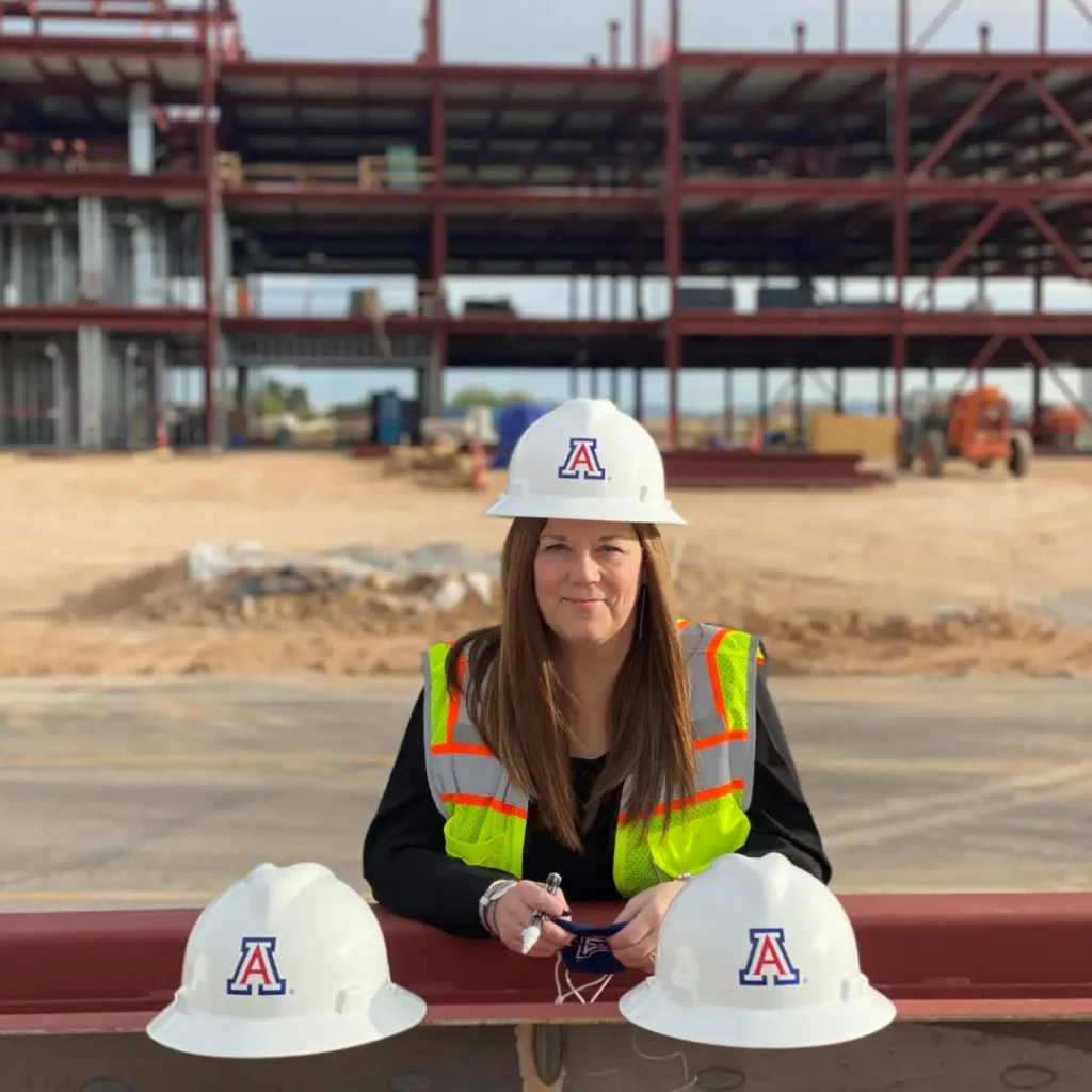 A CEO, wearing a hard hat with the University of Arizona logo and a safety vest, signs the final steel beam of the newly constructed building, marking a milestone in its completion.