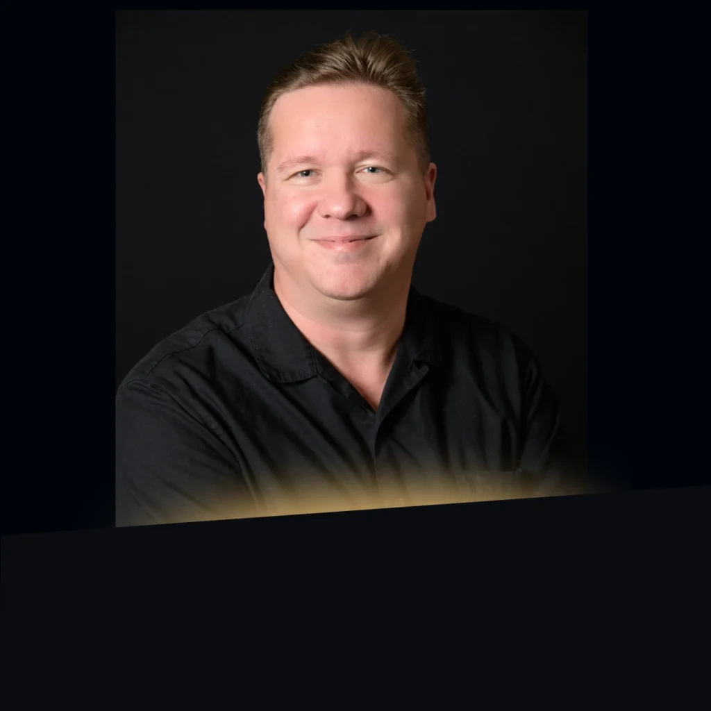 Headshot of Craig Klein wearing a black button down with gold glow at the bottom