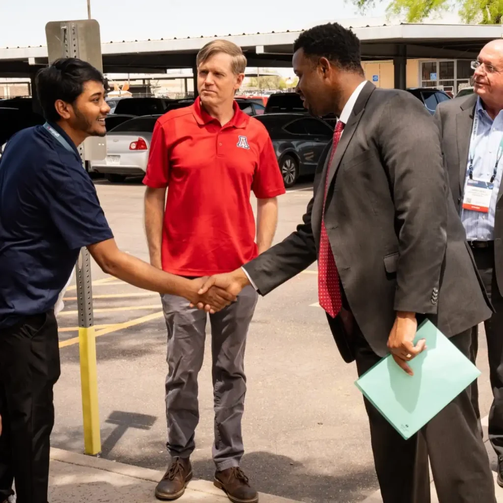 Two professionals shaking hands with man in red U of A shirt in the middle