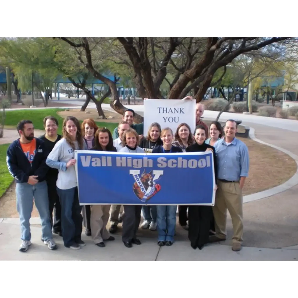 Group of Vail High School staff and supporters holding a banner and thank you sign outdoors.