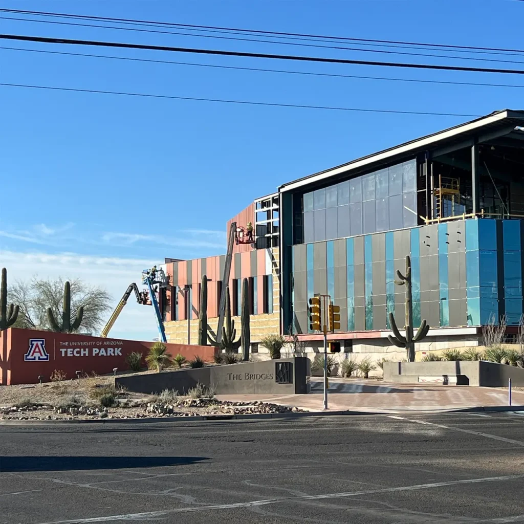 Modern building under construction with colorful panel siding and large glass windows, surrounded by desert landscaping and saguaro cacti.