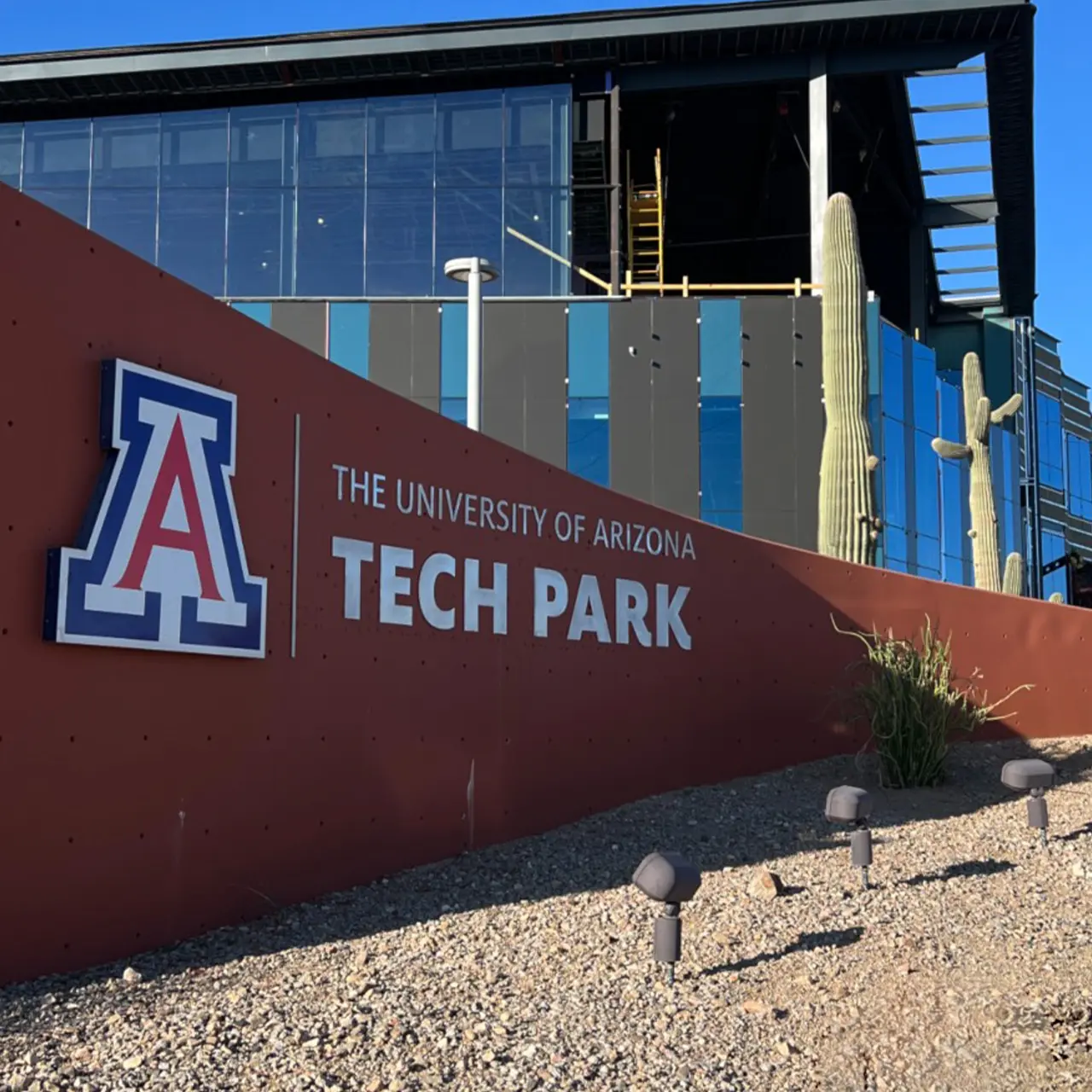 The University of Arizona Tech Park sign on light brown monument sign with building during construction behind.