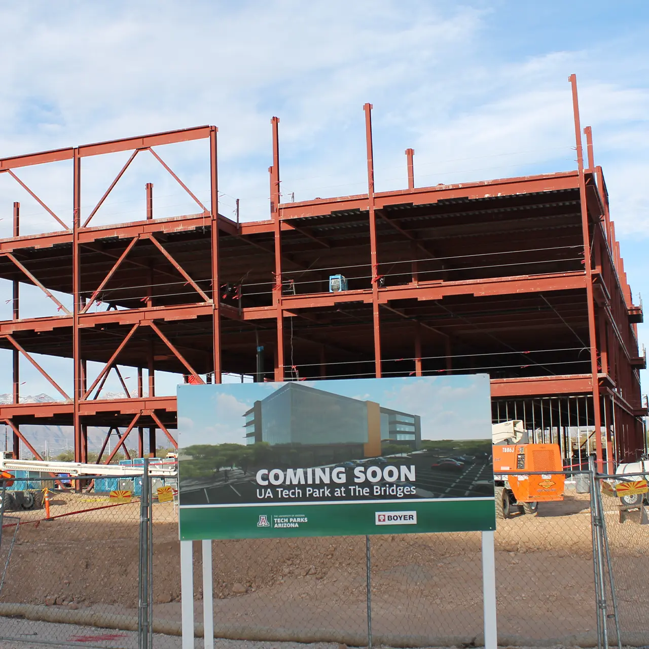 Steel-framed building under construction with a sign in front reading “Coming Soon: UA Tech Park at The Bridges.”