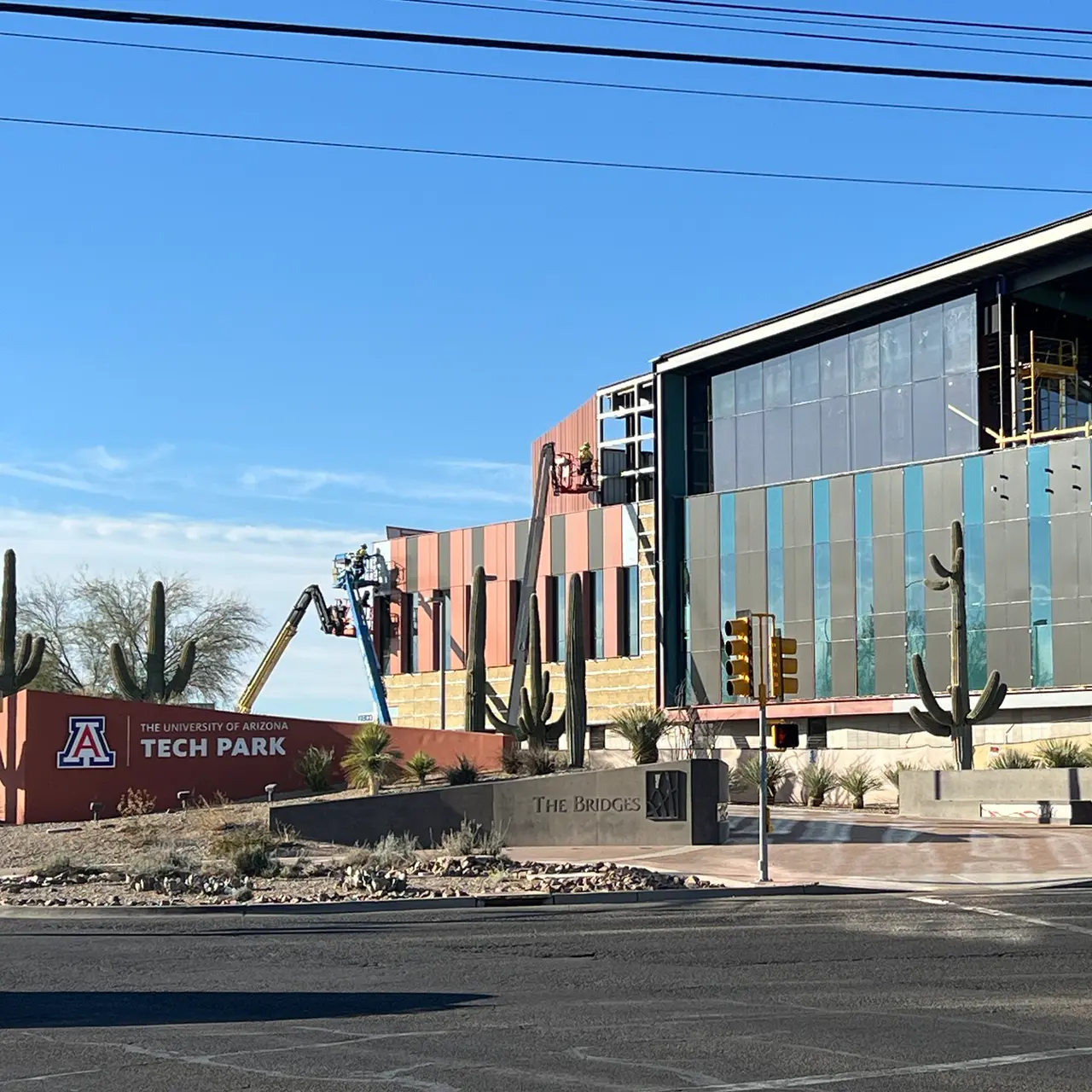 Modern building under construction with colorful panel siding and large glass windows, surrounded by desert landscaping and saguaro cacti.