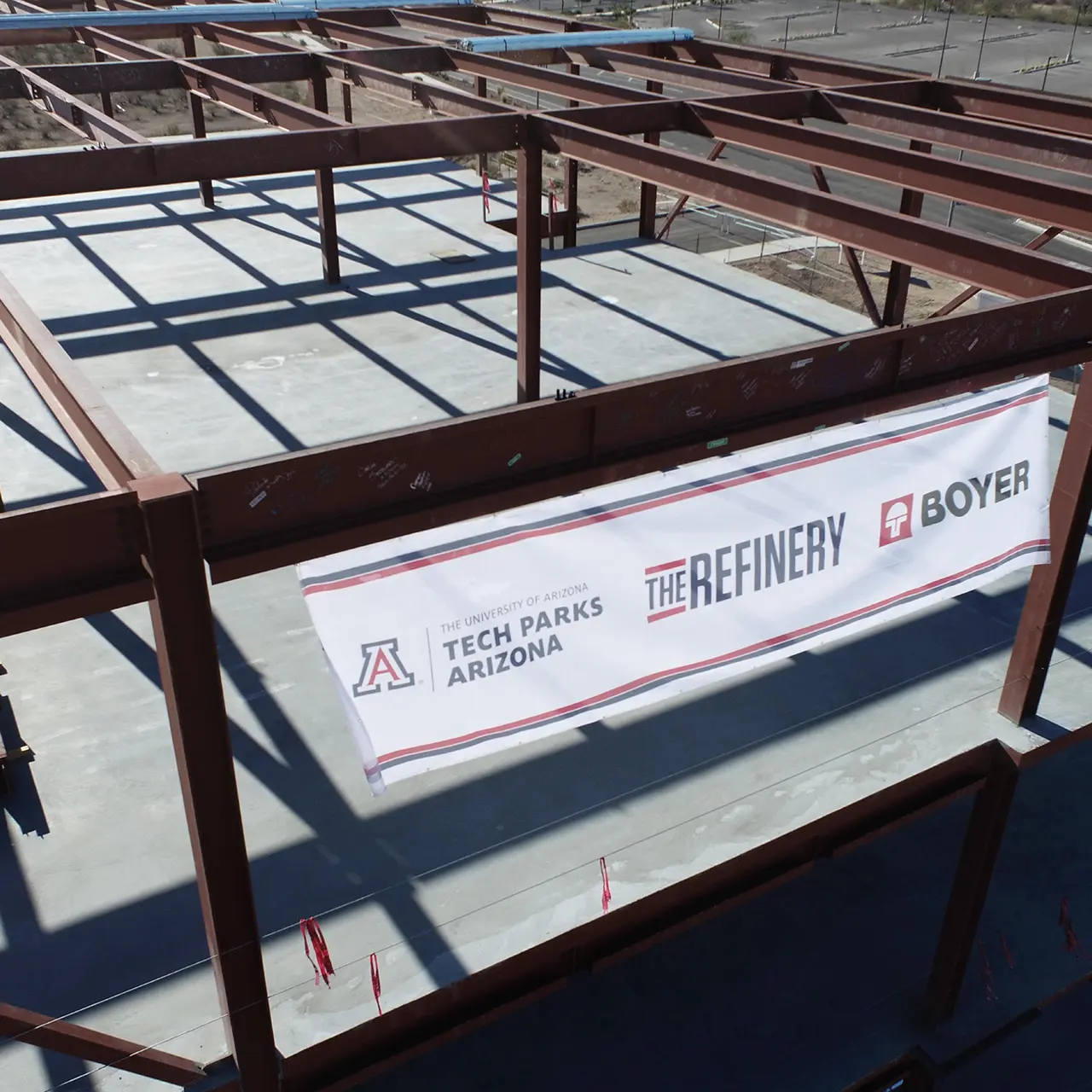 Construction beams with white banner hanging with three logos: Tech Parks Arizona, The Refinery, and Boyer.