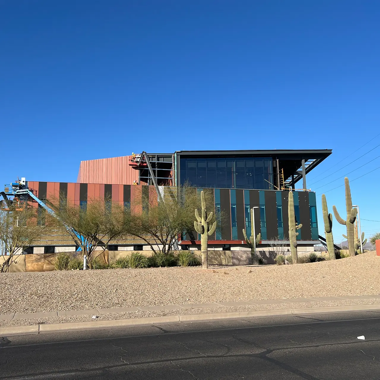 Modern building under construction with colorful panel siding and large glass windows, surrounded by desert landscaping and saguaro cacti.