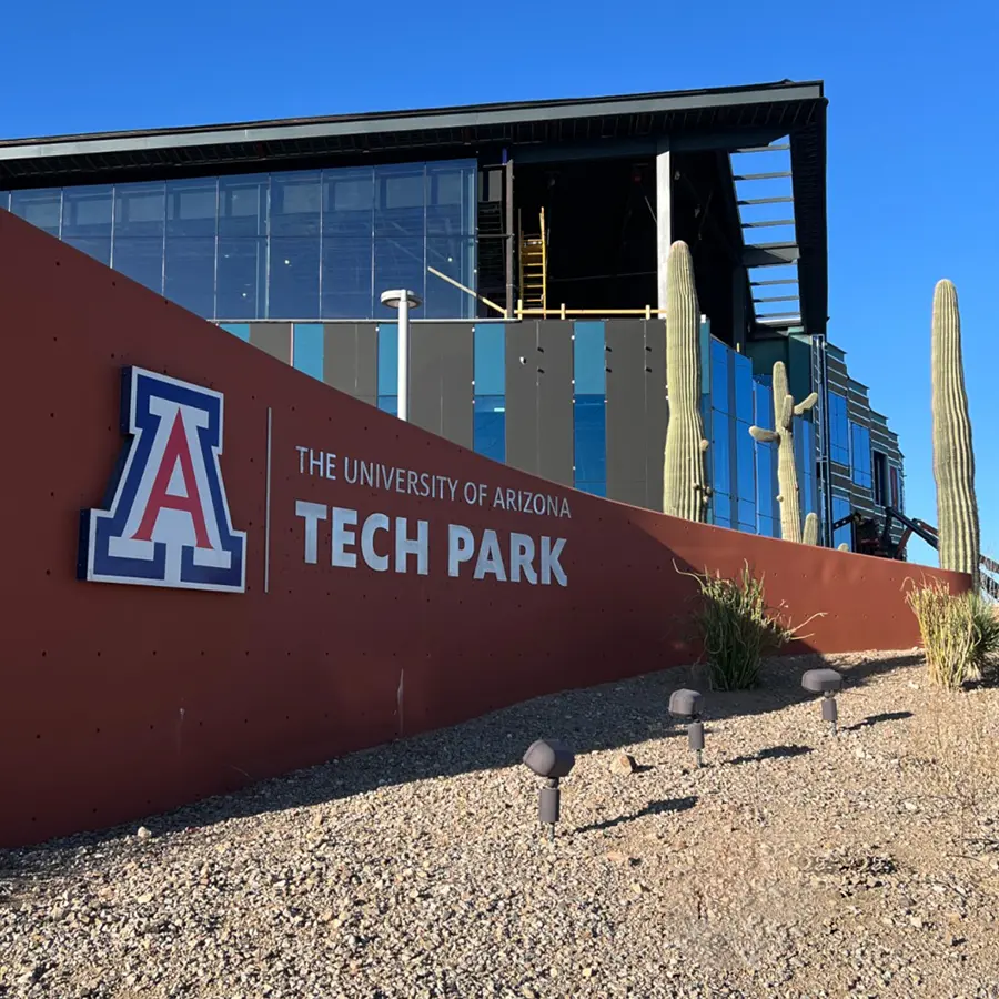 The University of Arizona Tech Park sign on light brown monument sign with building during construction behind.