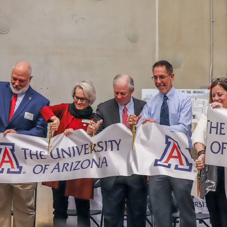 Group of five people cutting a large University of Arizona ribbon with gold scissors.