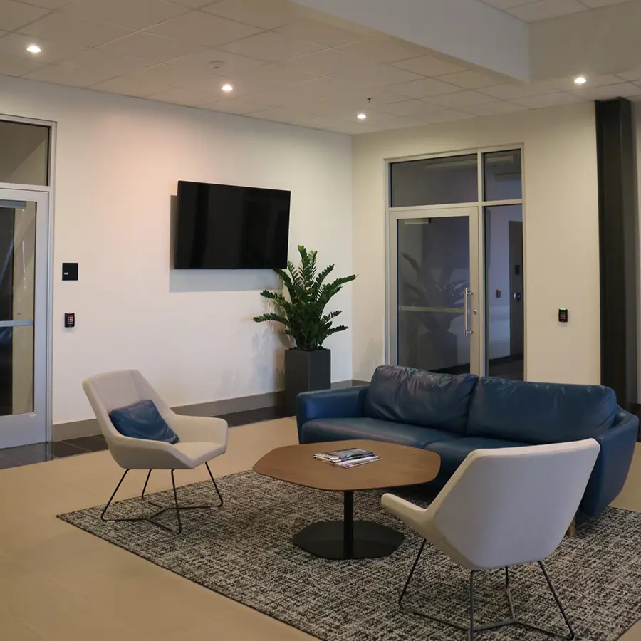Modern office lounge with a blue couch, two chairs, a coffee table, and a wall-mounted TV.
