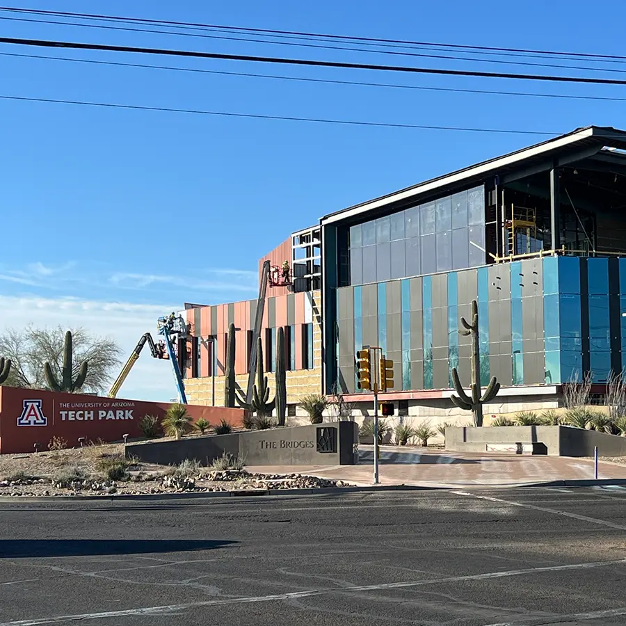 Modern building under construction with colorful panel siding and large glass windows, surrounded by desert landscaping and saguaro cacti.
