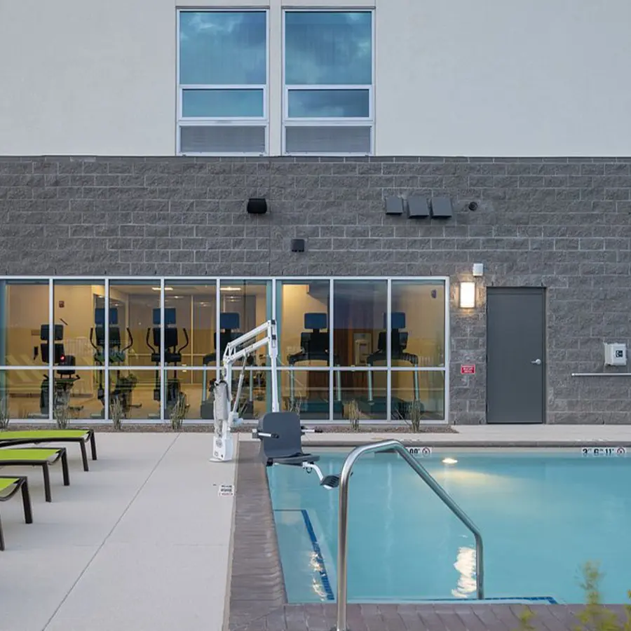 Hotel pool with green chairs and windows looking into gym.