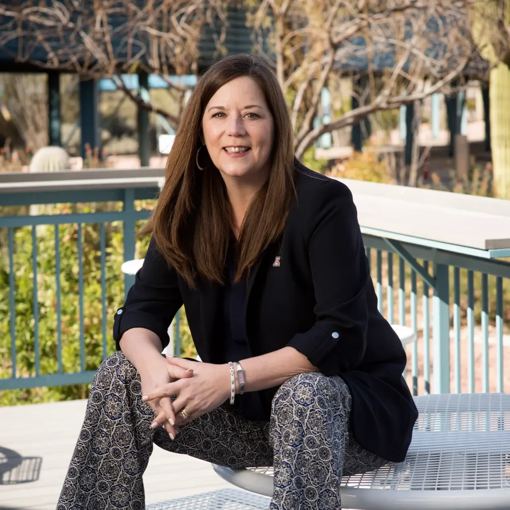 Professional woman posing for photo while sitting outside on a table.