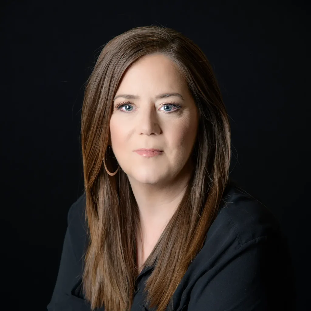 Headshot of woman wearing black top in front of black background.
