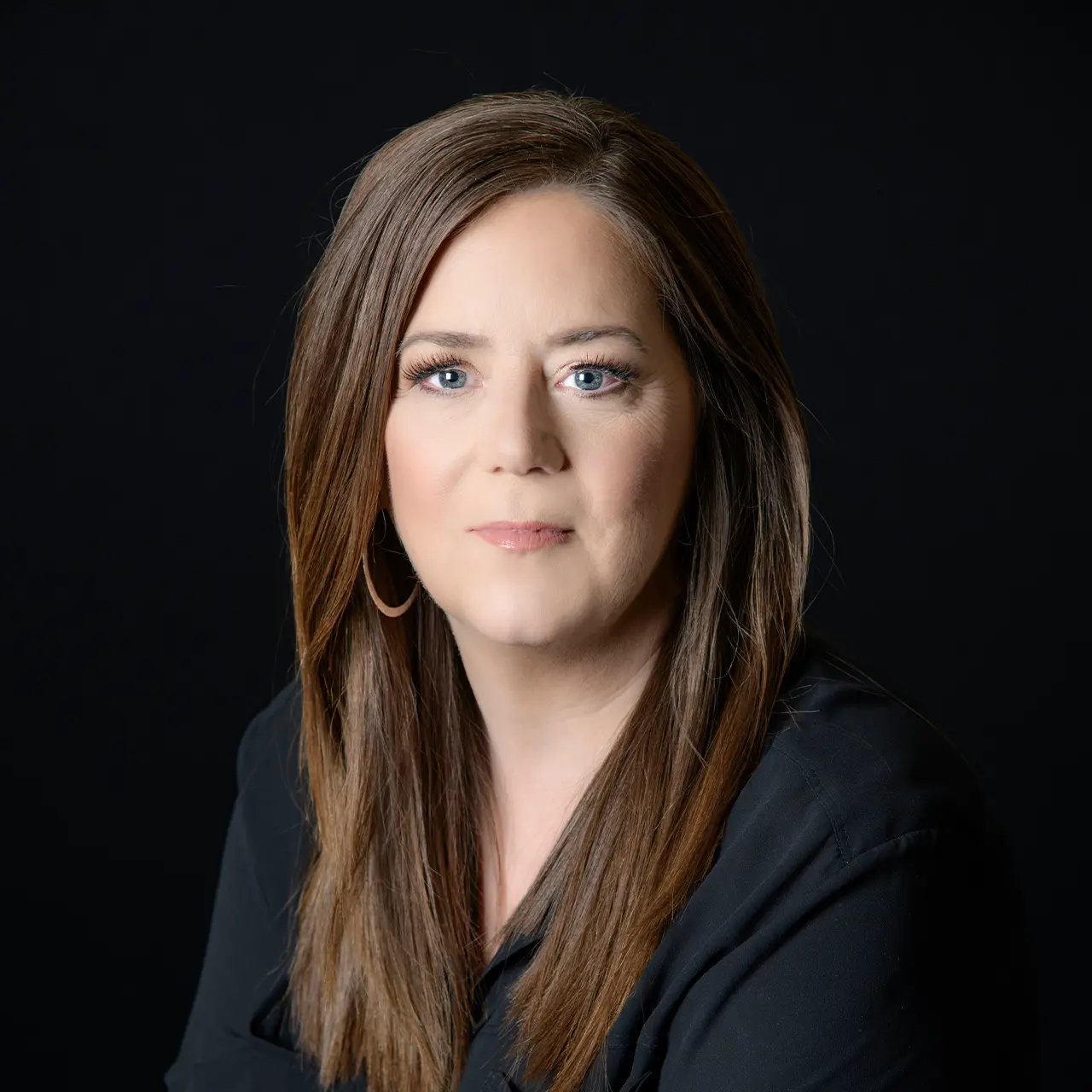 Headshot of woman wearing black top in front of black background.