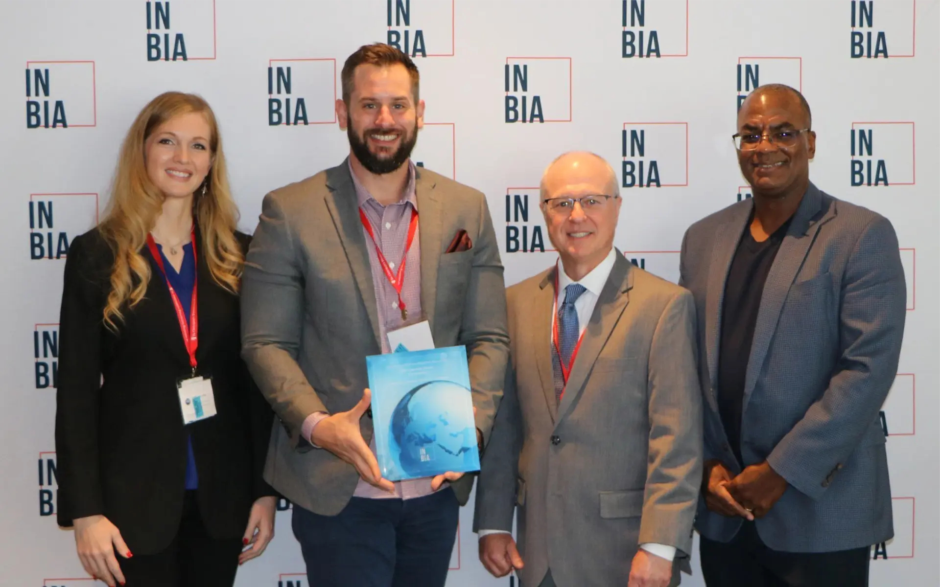 Four people dress professionally standing in front of IN BIA backdrop posing for a photo.