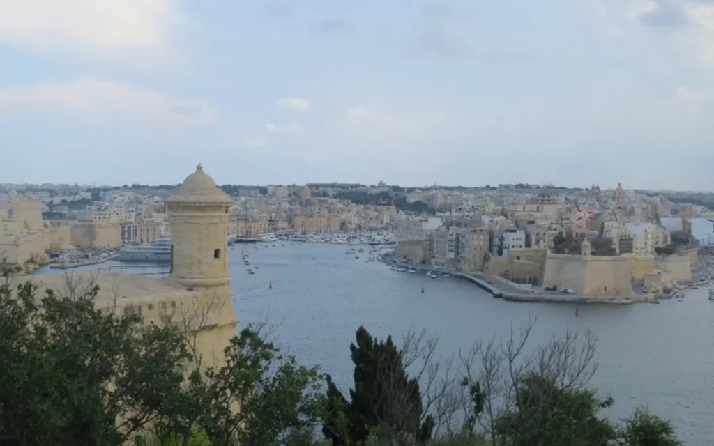 View of Grand Harbour and historic fortified city of Valletta, Malta, with stone watchtower in foreground.