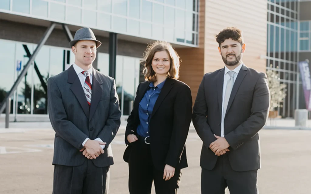 Three people dress professionally posing for a photo in front of a building.