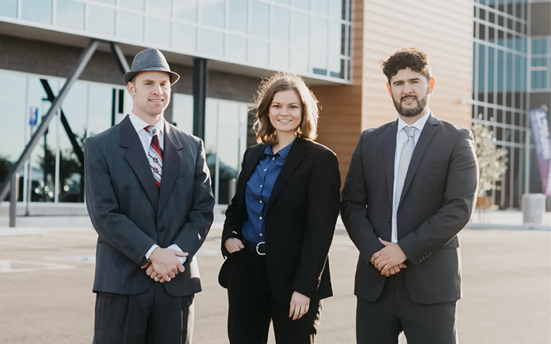 Three people dress professionally posing for a photo in front of a building.