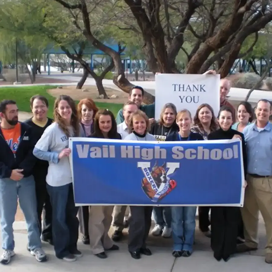 Group of Vail High School staff and supporters holding a banner and thank you sign outdoors.