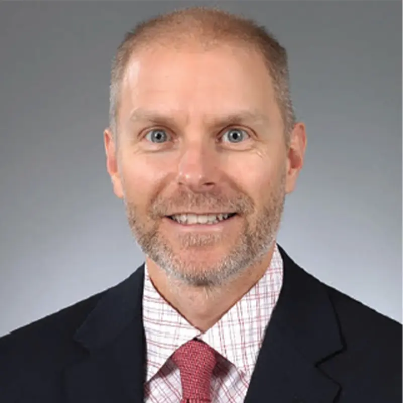 Headshot of Ryan Goodell wearing a black suit and red tie.