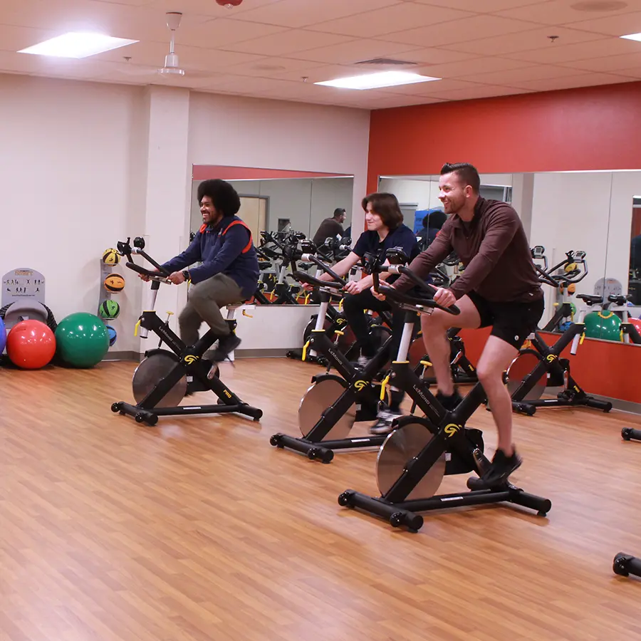 Three people on electric bikes in a fitness room.