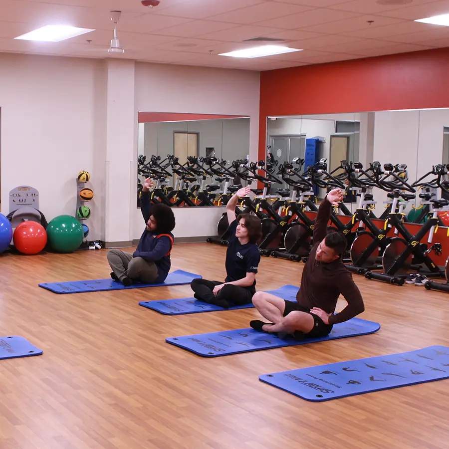 Three people stretching on yoga pads in an exercise room.