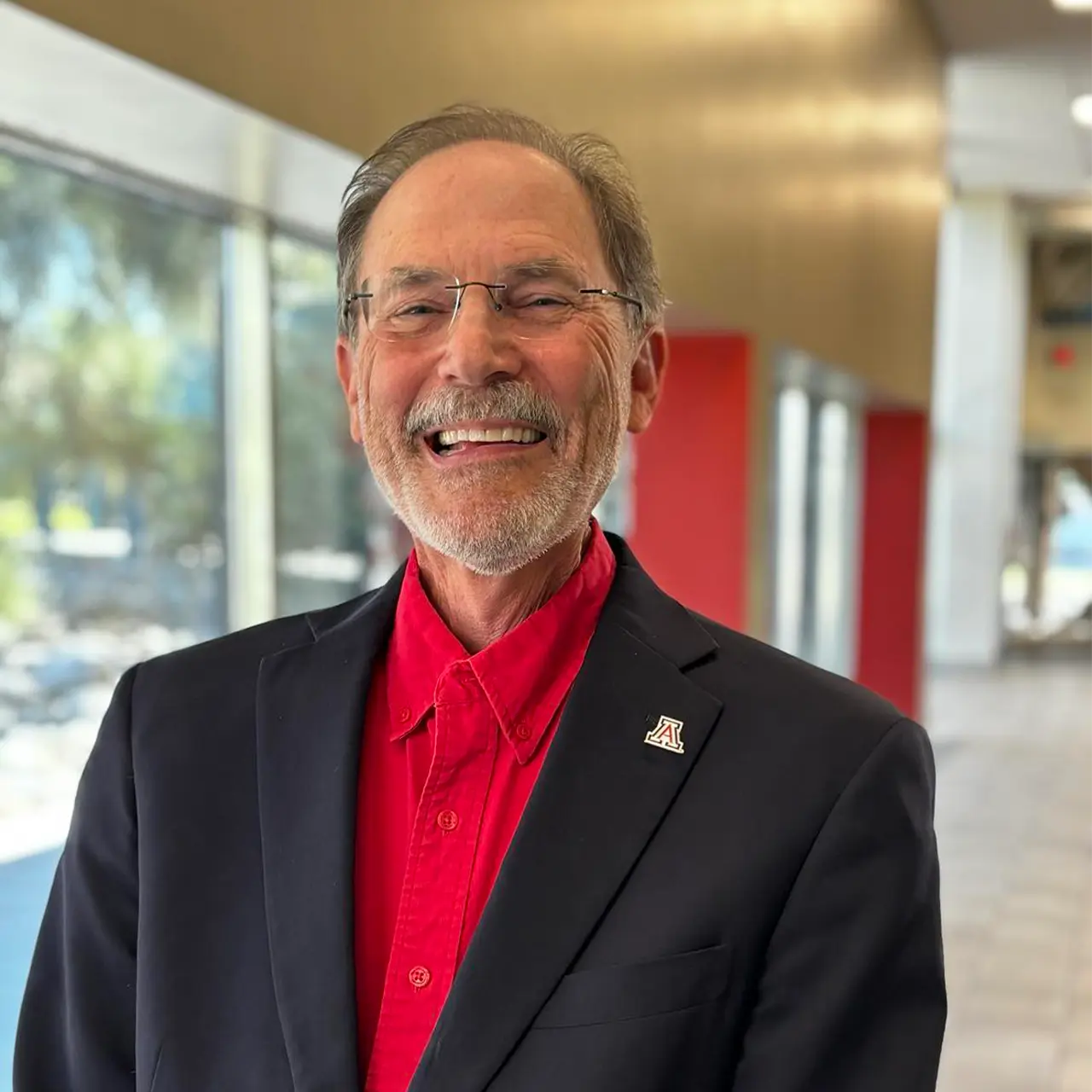 Man smiling wearing a red button down and black blazer with University of Arizona pinned on blazer.