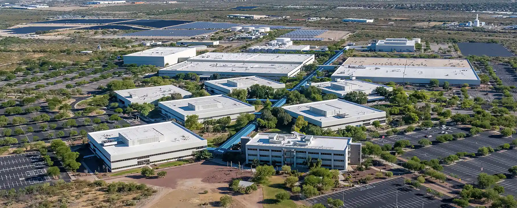 Aerial view of a large, modern business and research park with multiple buildings, tree-lined walkways, and surrounding parking lots.