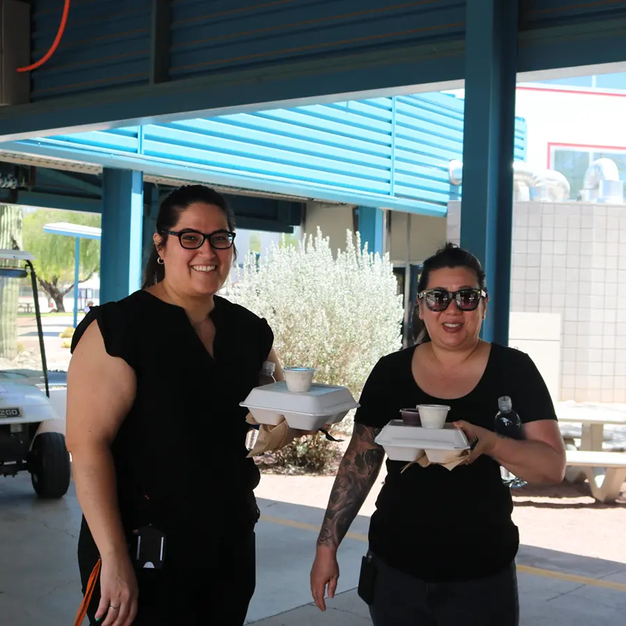 Two women smiling for photo holding to-go boxes.