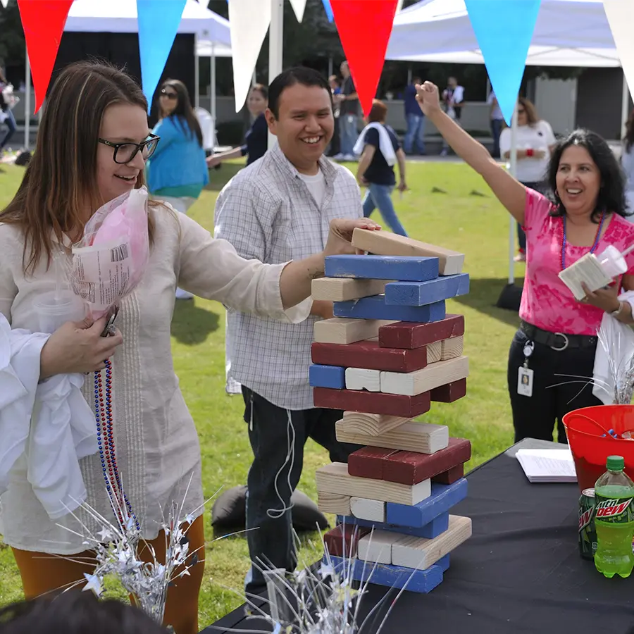 Woman playing jenga at an outdoor event with two people cheering in the back.