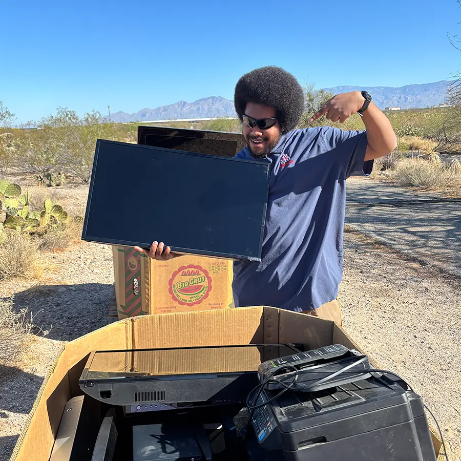 Man posing with a television behind a bin of donations.