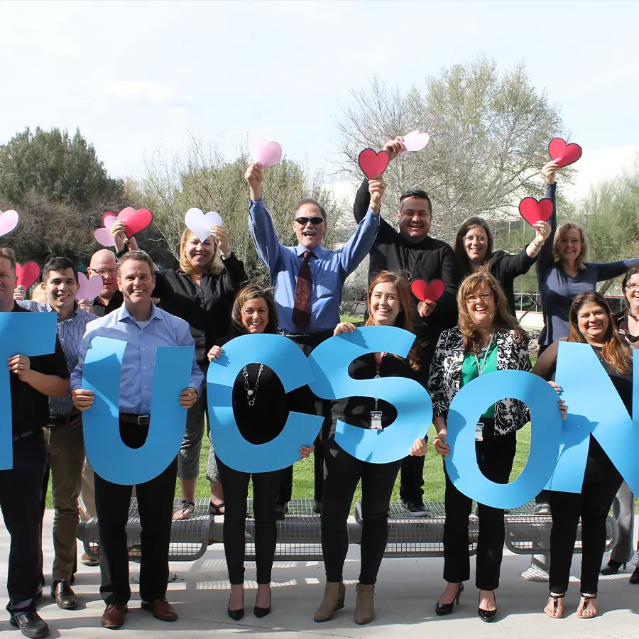 Group of people excitingly posing for a photo holding up letters to spell out "Tucson" and small hearts.