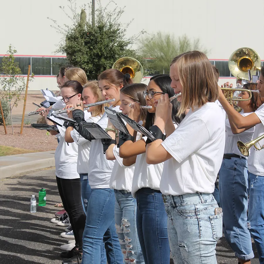 People in white t-shirts and jeans playing various instruments at an outside event.