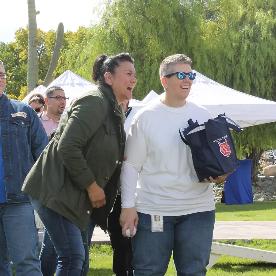 Two people smiling and enjoying themselves at an outdoor event, one carrying a blue bag with Tech Cats logo.