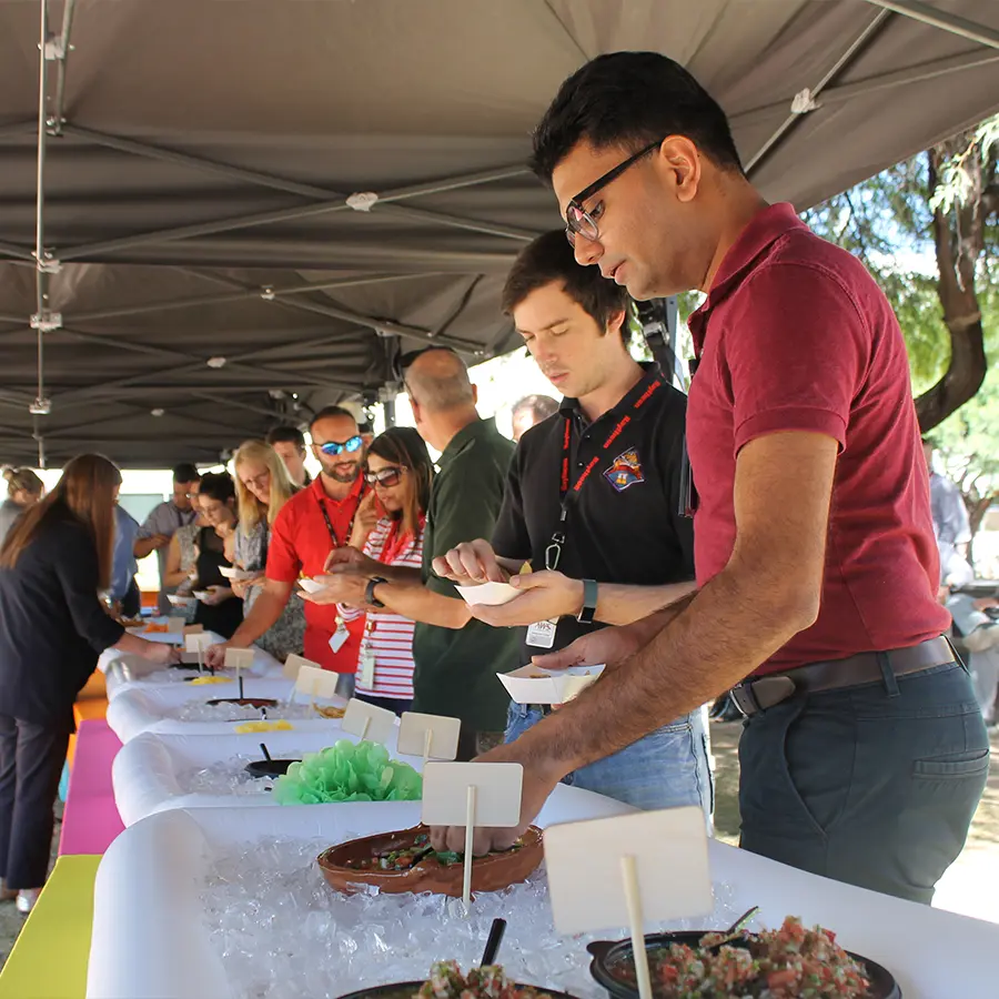 People serve themselves food from a buffet line under an outdoor event tent.