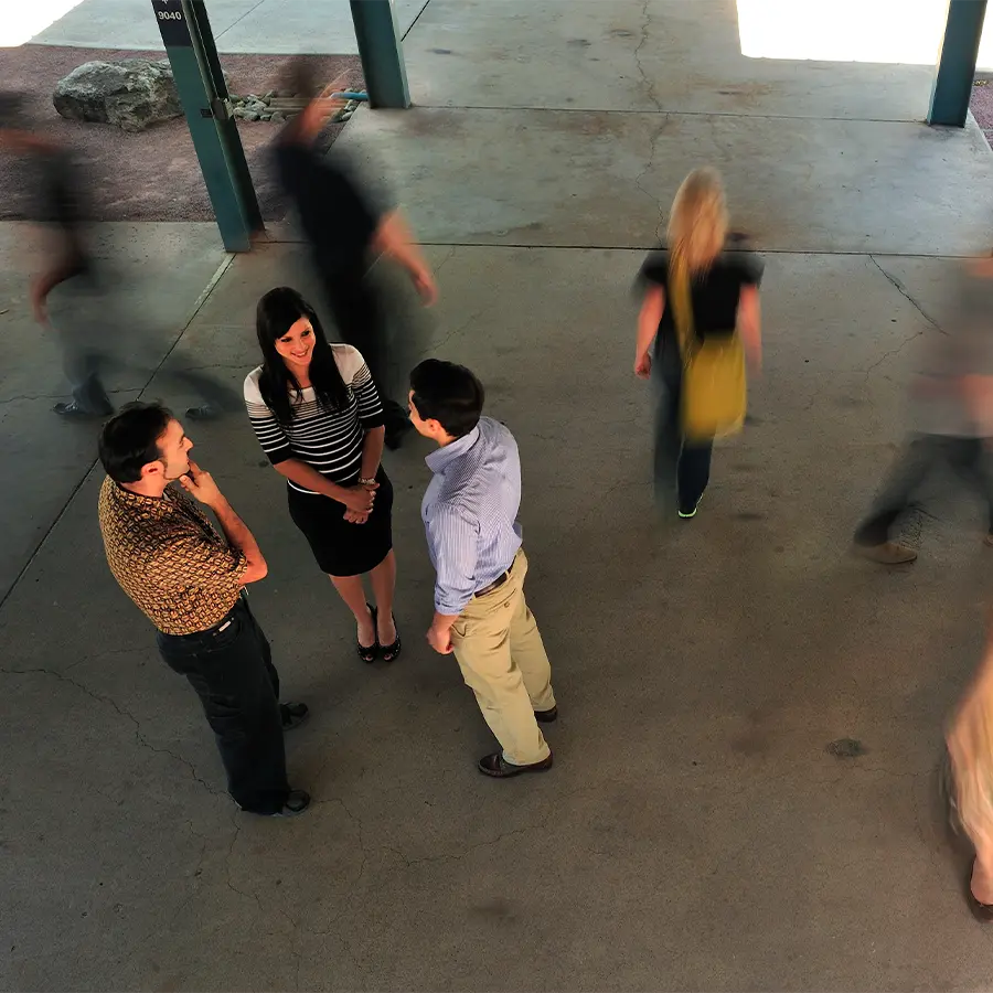 Three people standing in circle talking on a busy walkway.