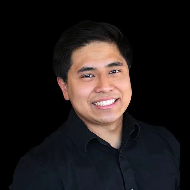 Smiling man with short dark hair wearing a black button-up shirt against a dark background.