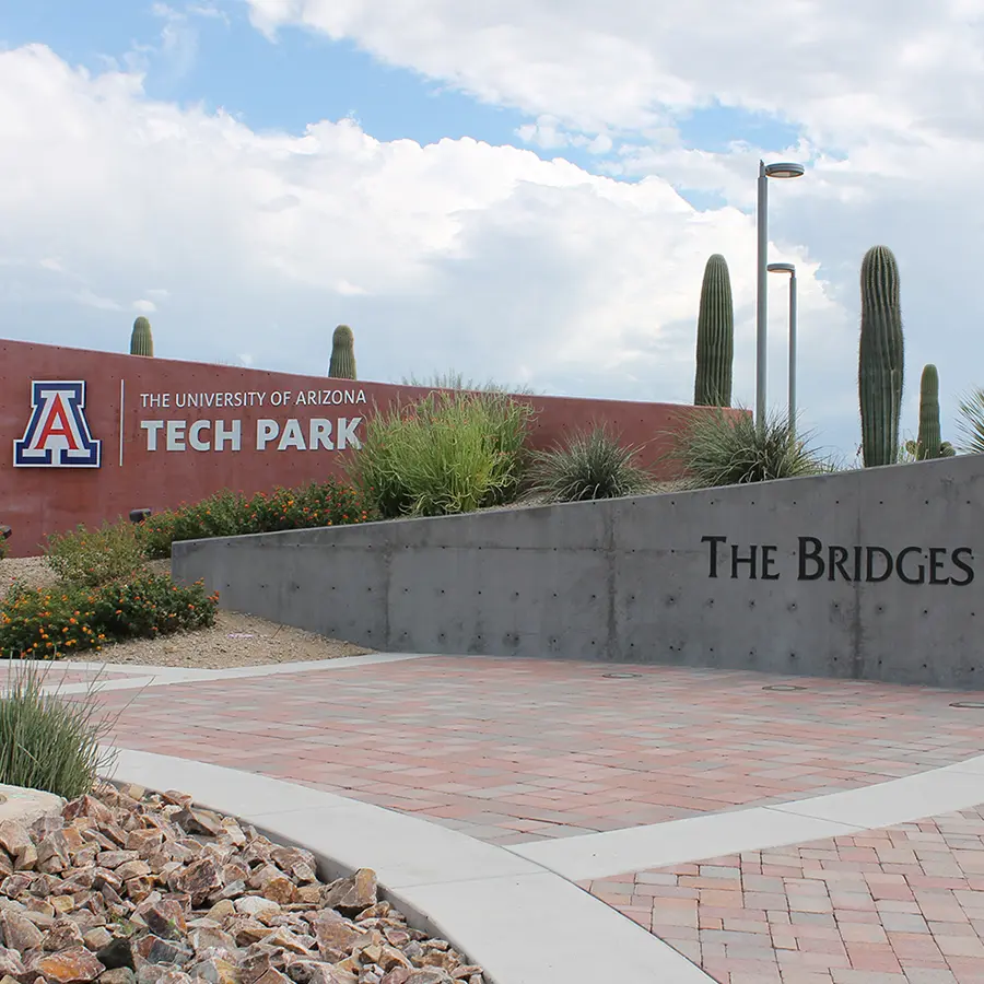 Entrance sign for the University of Arizona Tech Park at The Bridges, featuring desert landscaping and iconic saguaros.