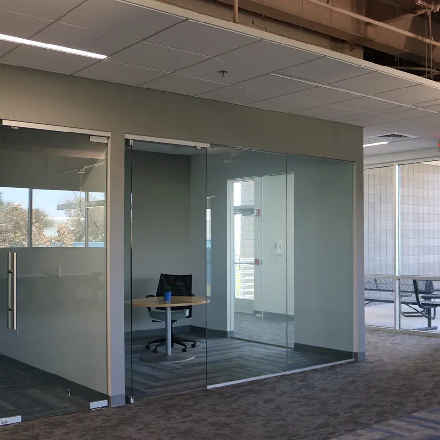 Office with glass walls and a wood table and black chair.